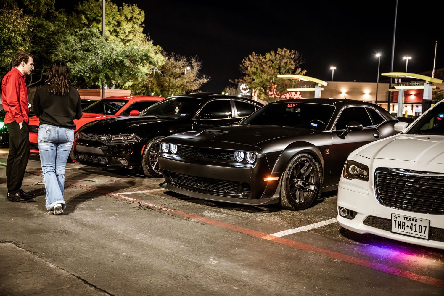 Custom performance cars lined up at night in a parking lot with under-glow lighting.