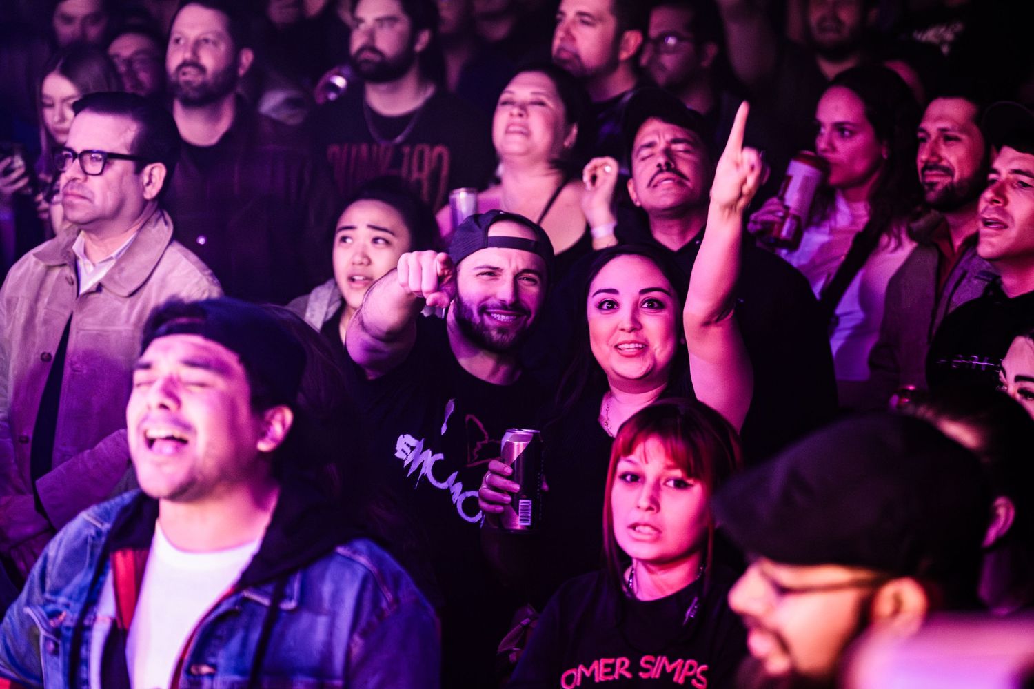 Energetic crowd watching and cheering at a music concert under purple lights.