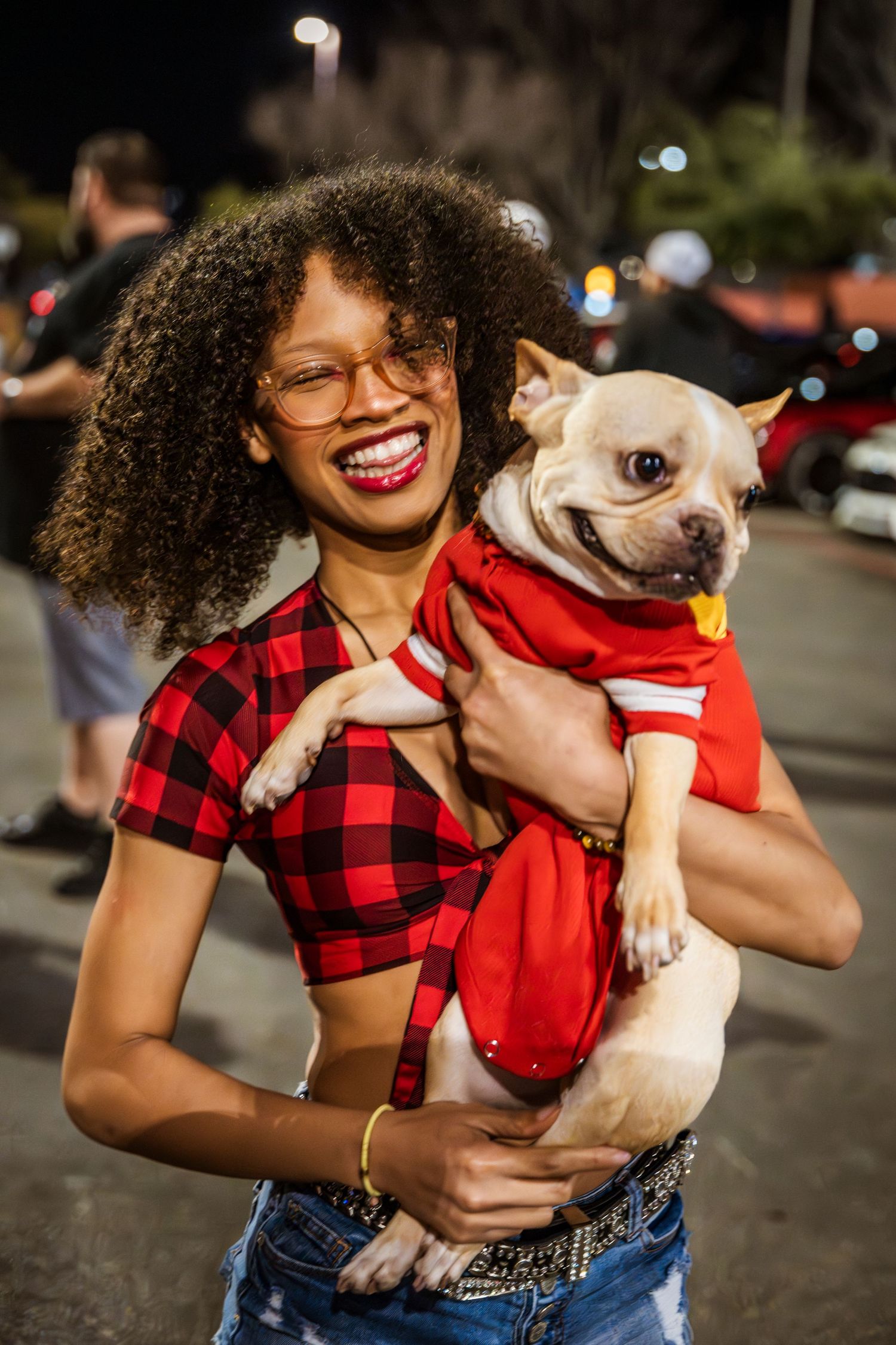 Person in buffalo plaid crop top holding smiling French Bulldog wearing red shirt.