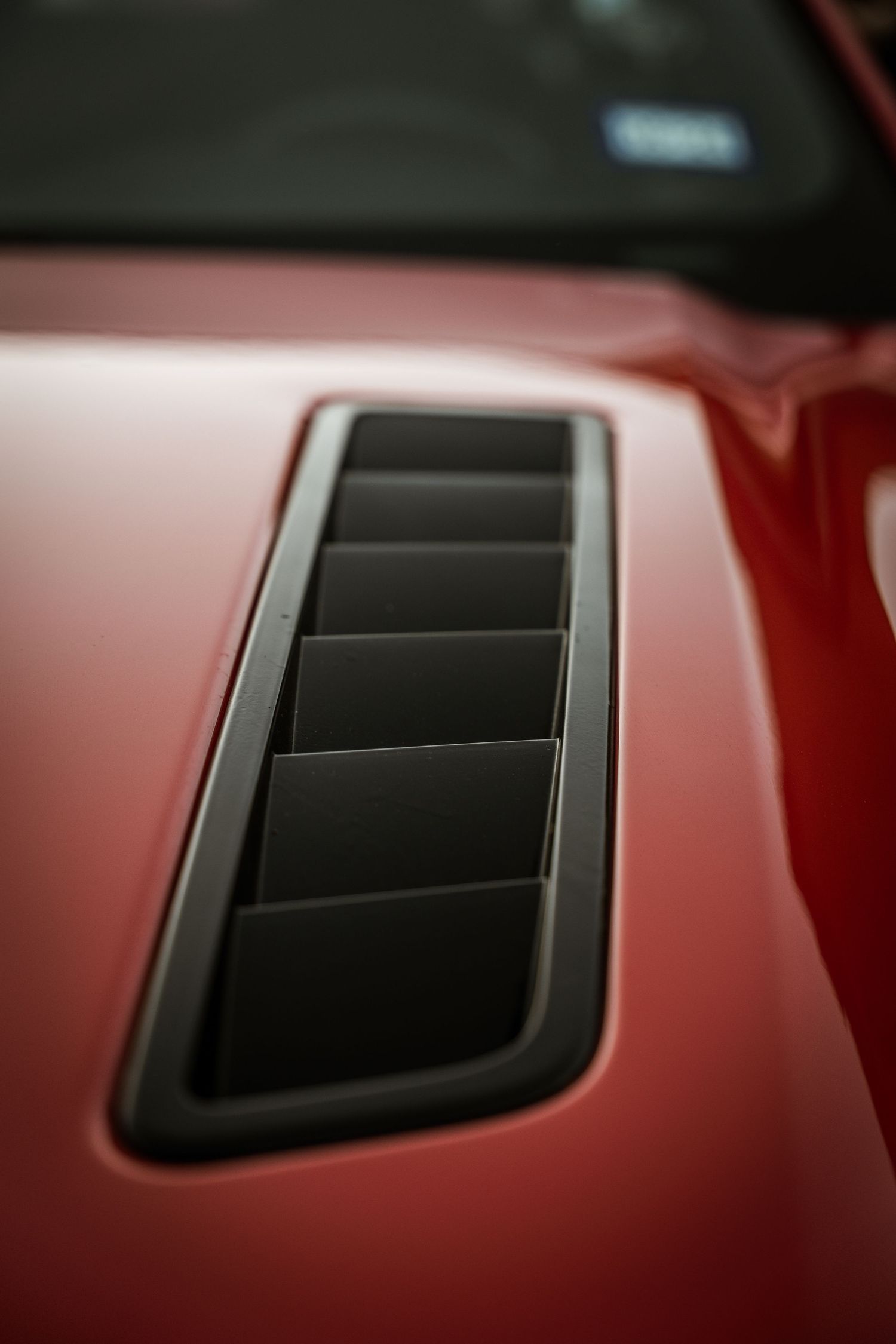 Close-up detail of a red car hood vent with black slats.