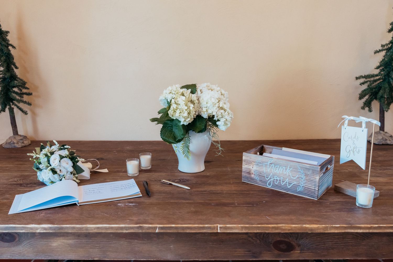 Wedding guest book table decorated with white flowers, wooden box and writing materials.
