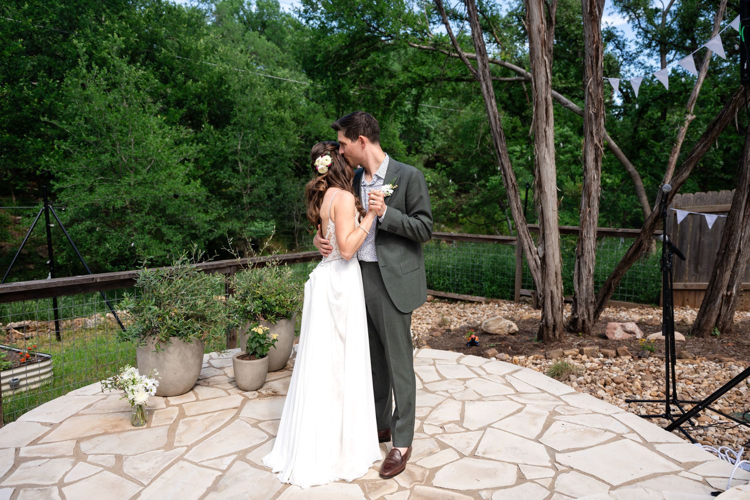 A wedding couple sharing an intimate moment on a stone patio surrounded by greenery.