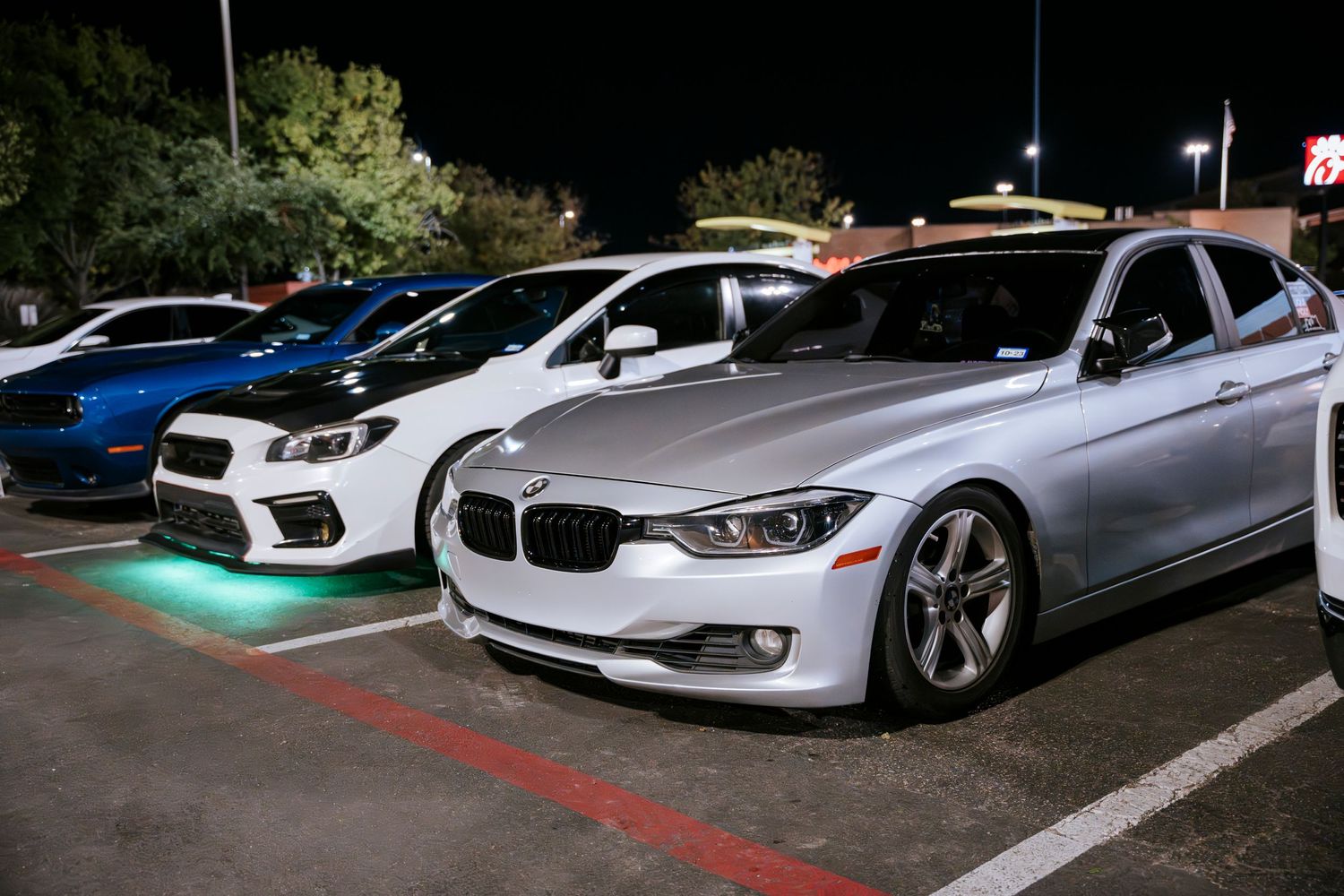 Modified BMW 3-series and Subaru WRX parked side by side in a nighttime lot.