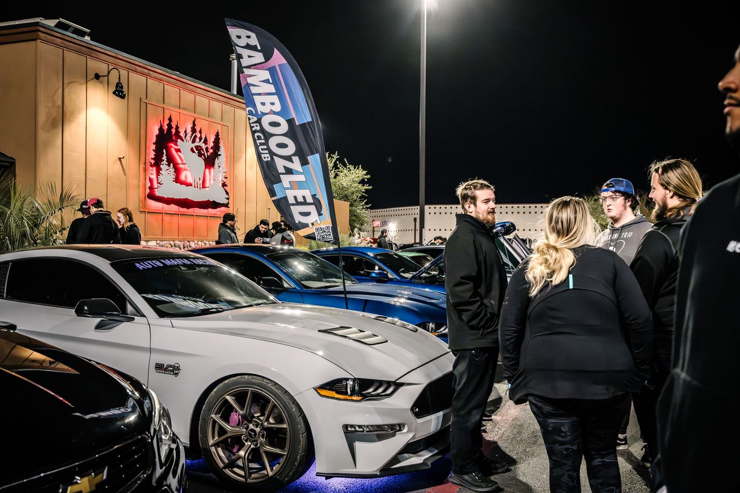 Car enthusiasts gathered around modified vehicles at nighttime outdoor event.