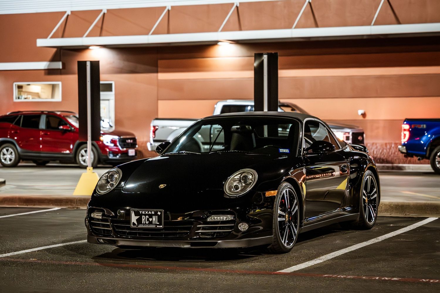 Black Porsche 911 parked under lights in parking structure.