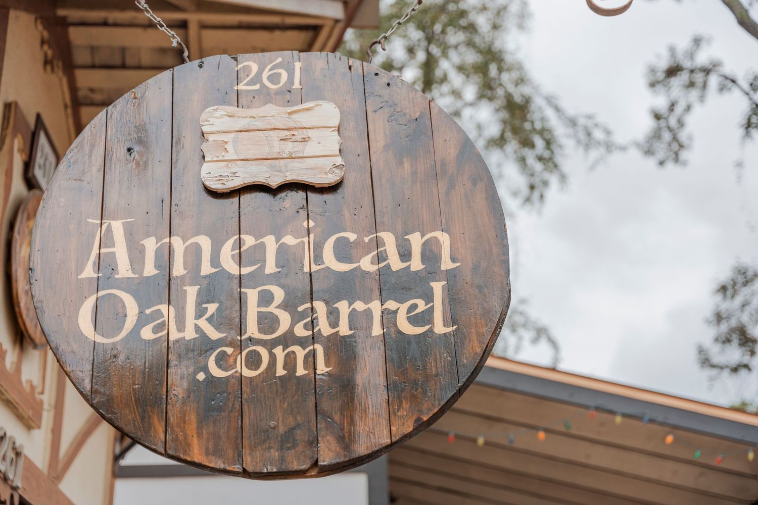 Wooden circular sign for American Oak Barrel mounted on a rustic building exterior.