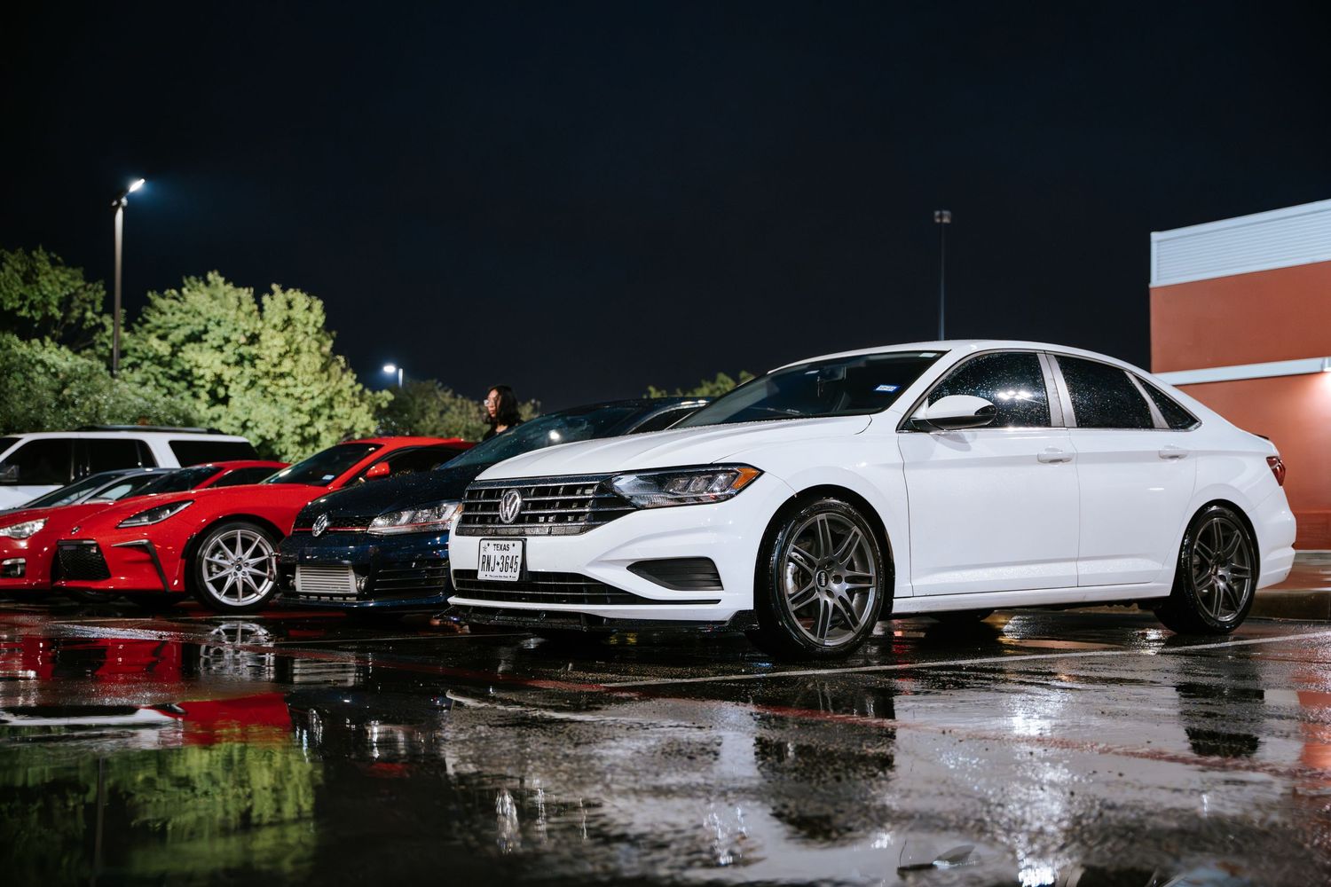 Row of modified white sedans displayed in a wet parking lot at night.