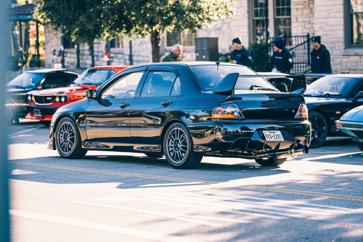 Modified black Mitsubishi Evo sports car with custom wheels parked on a street.