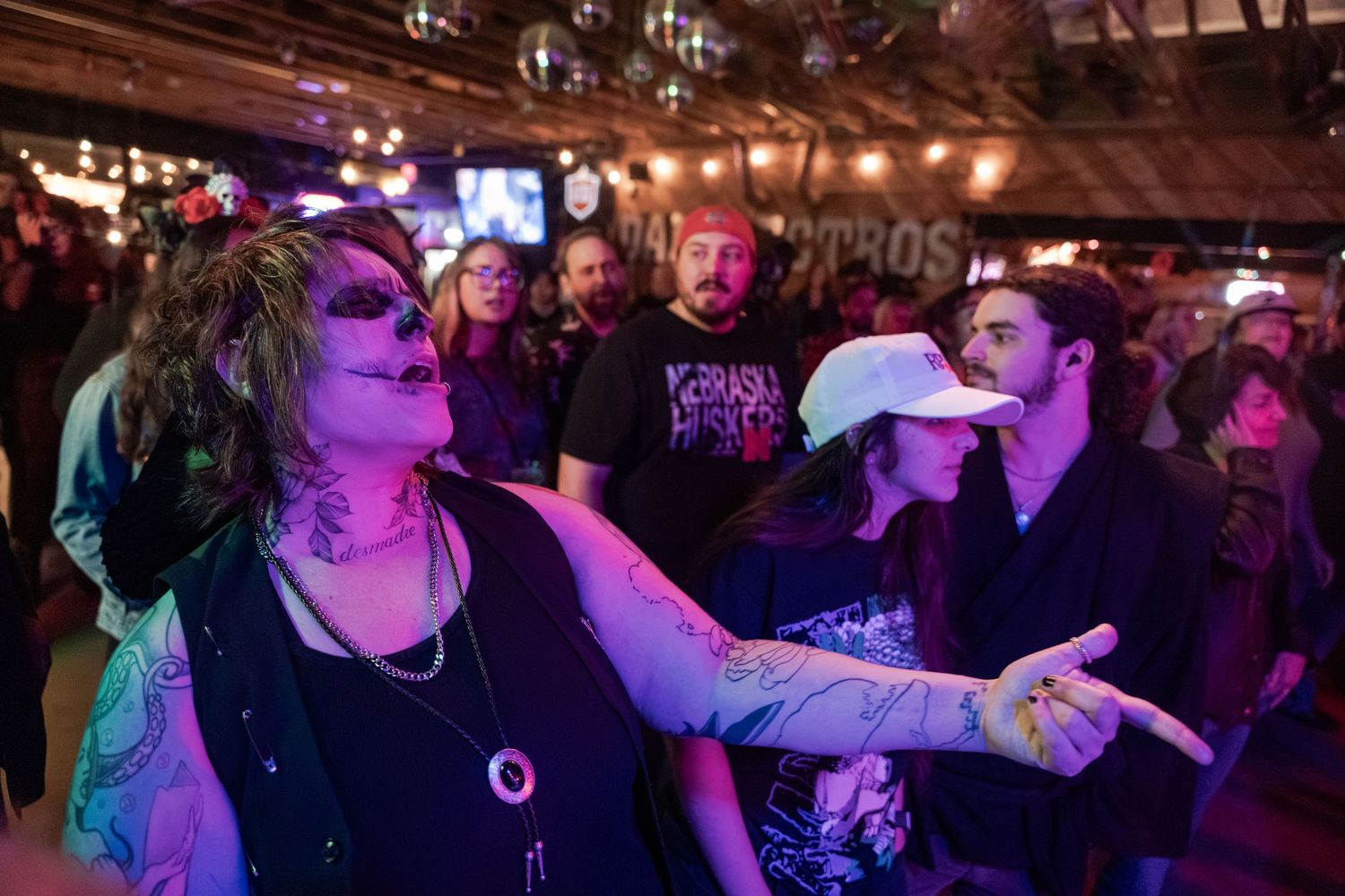 Energetic crowd enjoying live music at a dimly lit bar with purple lighting and exposed ceiling beams.