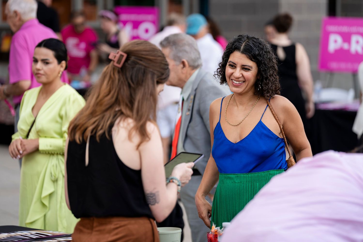 People gather outdoors at a social event with pink signage visible in the background.