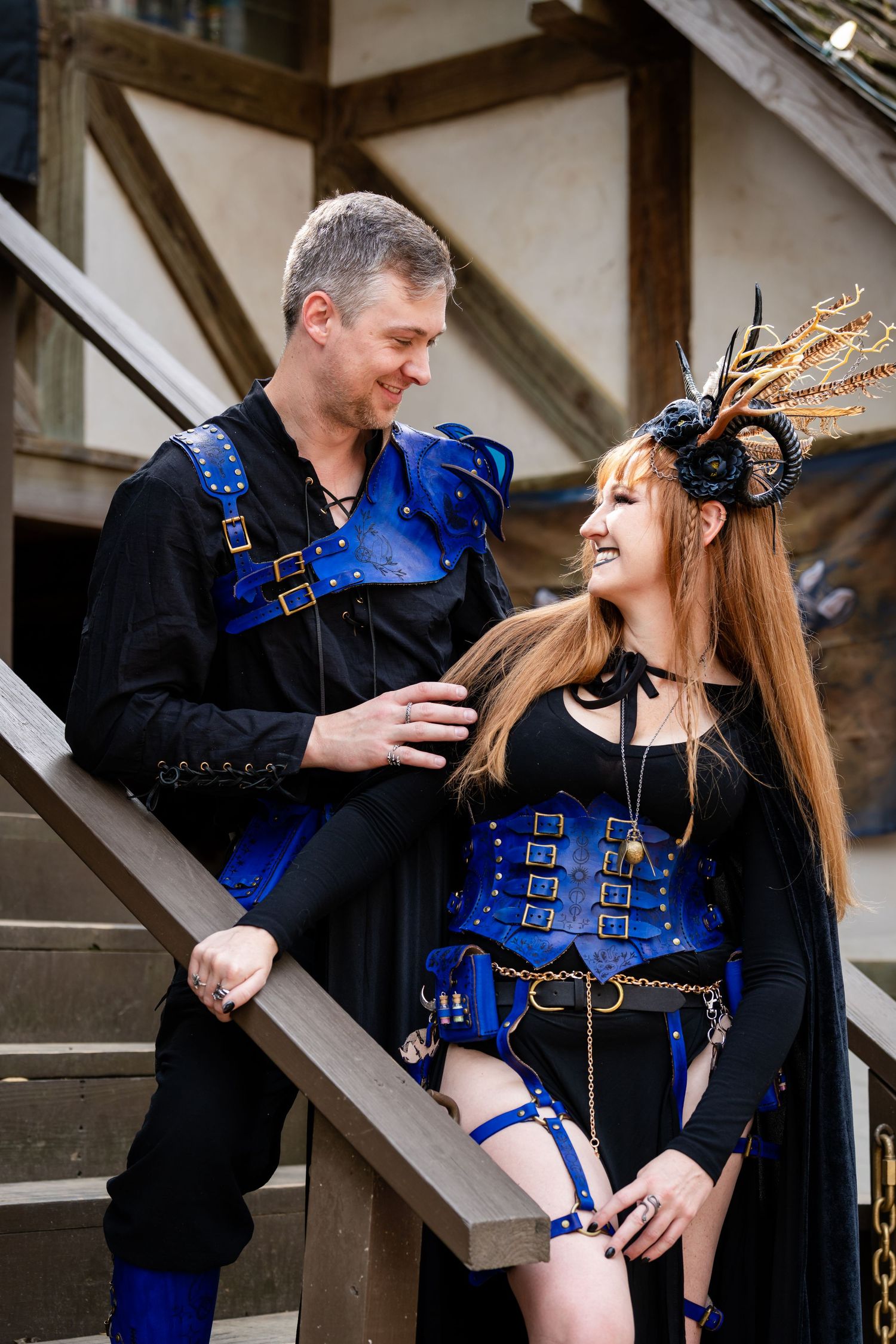 A couple in blue safety harnesses share an intimate moment while standing on metal stairs during an engagement photoshoot.