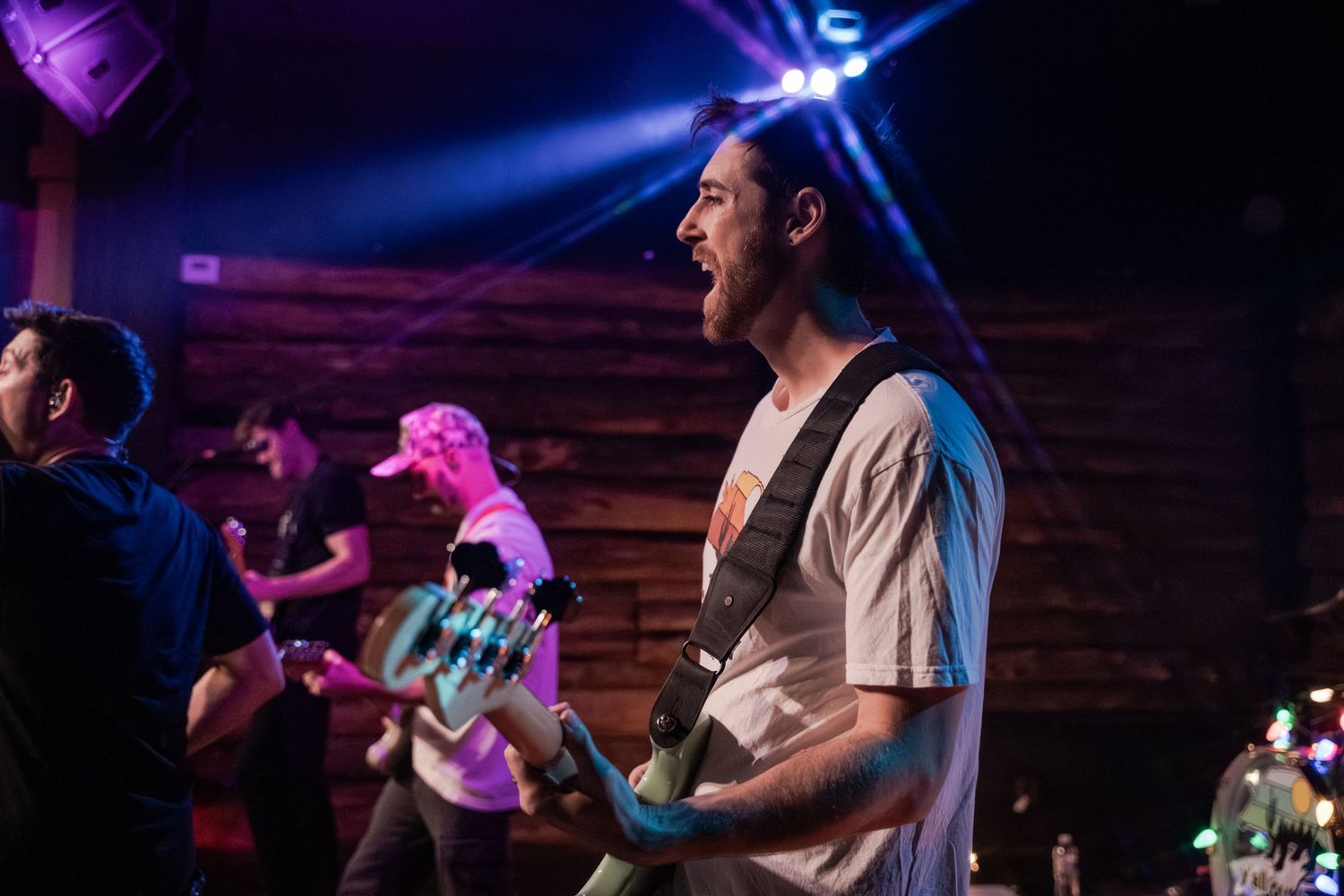Concert performers on stage illuminated by vibrant purple and blue lighting during an energetic live music performance.