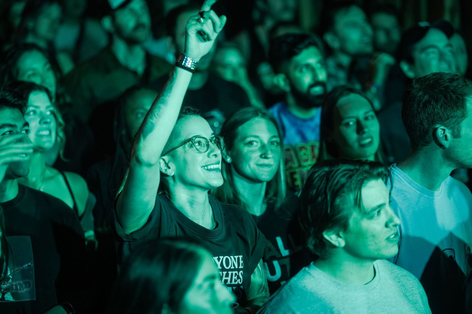 Concert crowd illuminated by teal blue lighting watches performance in a dark venue.
