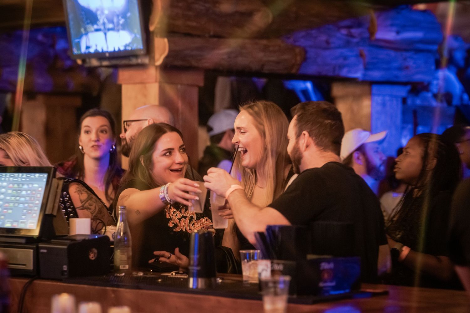 Friends enjoying drinks and conversation at a dimly lit bar with blue ambient lighting.
