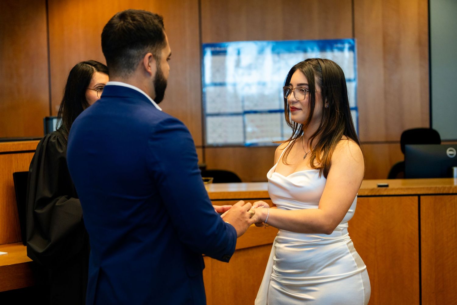 A couple exchanges vows during an intimate courthouse wedding ceremony in a wood-paneled room.