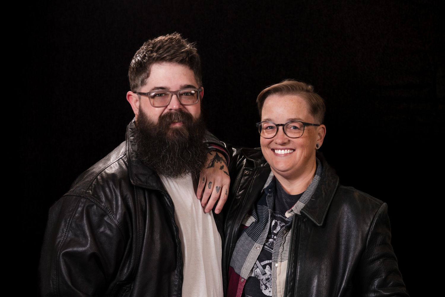 Two people in leather jackets and glasses smile together in a series of black and white photos.
