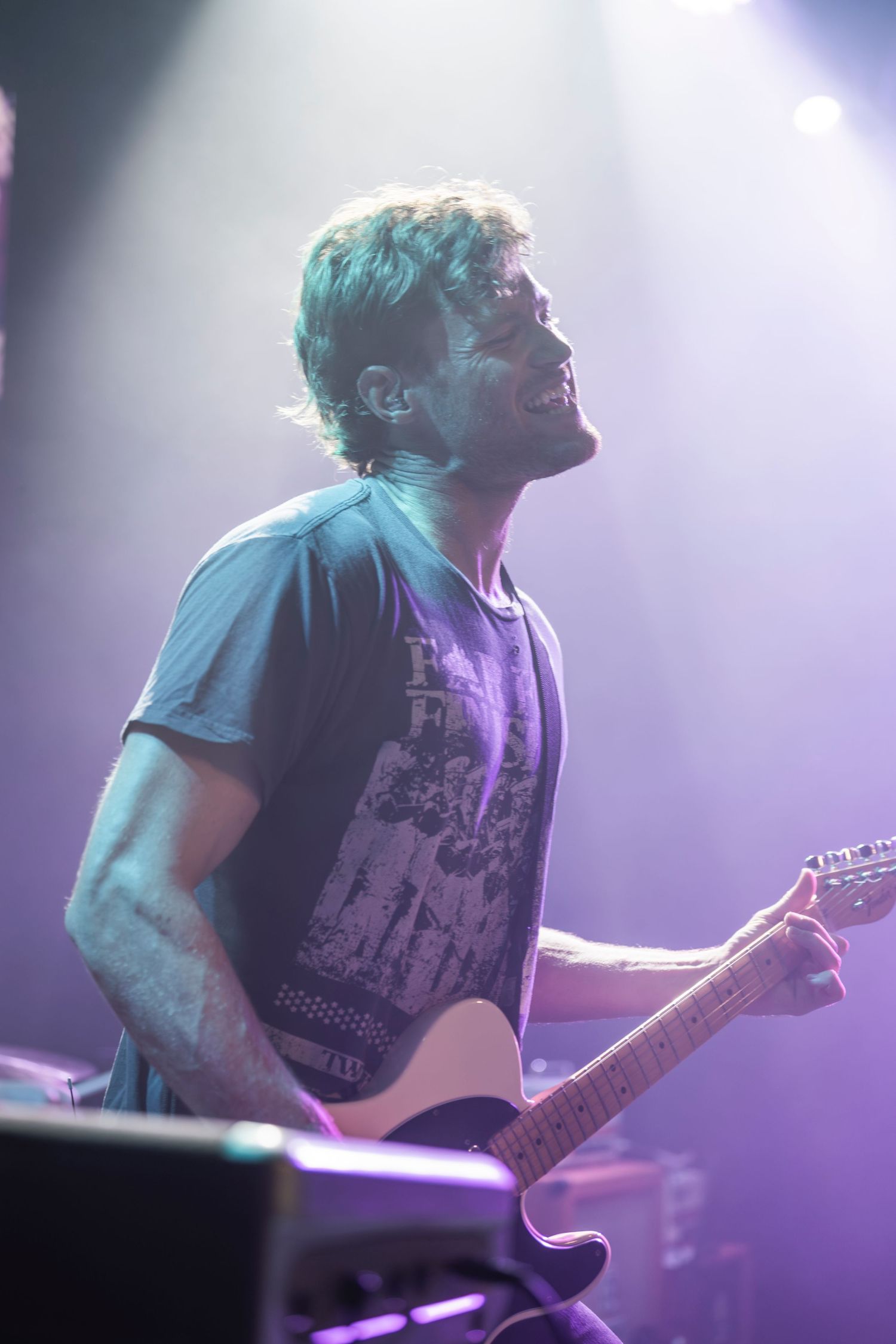 Musician playing electric guitar on stage bathed in dramatic purple stage lighting during live performance.