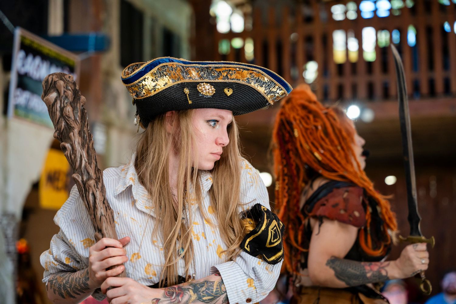 A person in an ornate pirate costume with a tricorn hat sits at a table in an atmospheric setting.