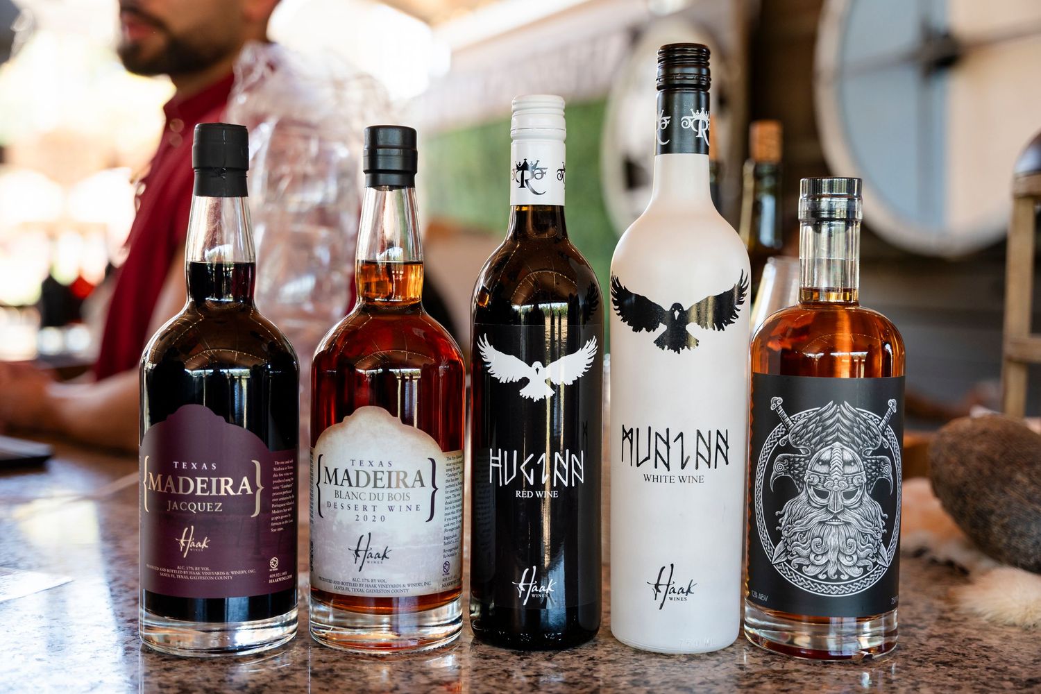 A row of assorted liquor and spirit bottles arranged on a wooden surface in a bar setting.