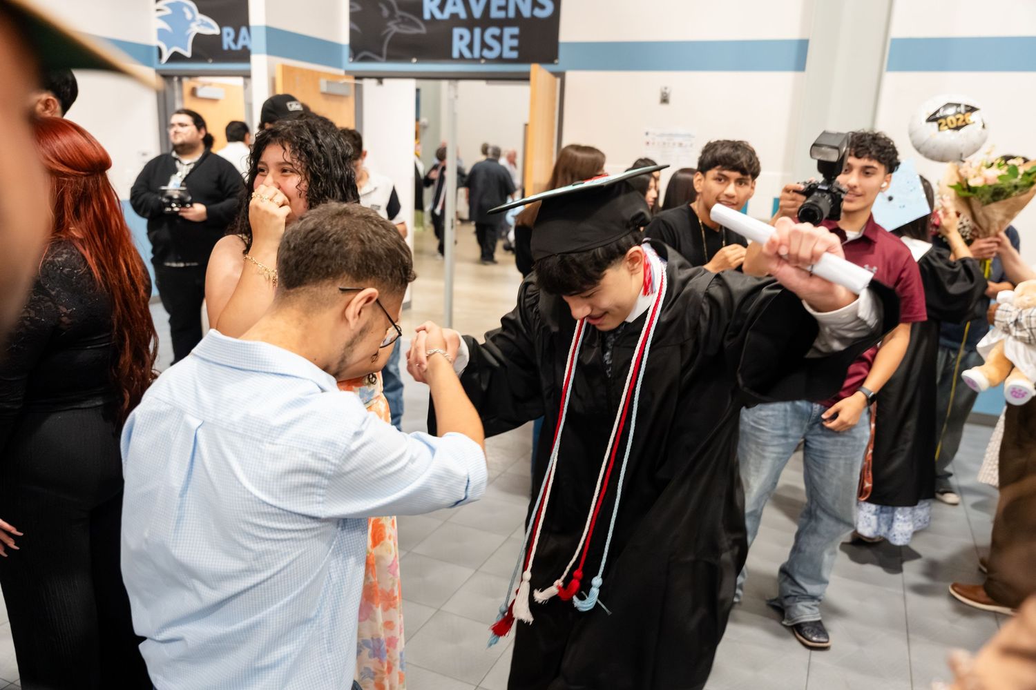 Graduate in cap and gown celebrates with family after commencement ceremony at Ravens Rise graduation event.