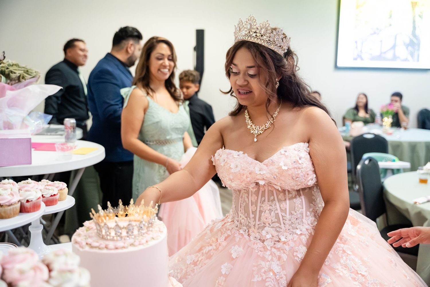 Young woman in pink quinceañera gown and tiara cutting her birthday cake at an elegant celebration.
