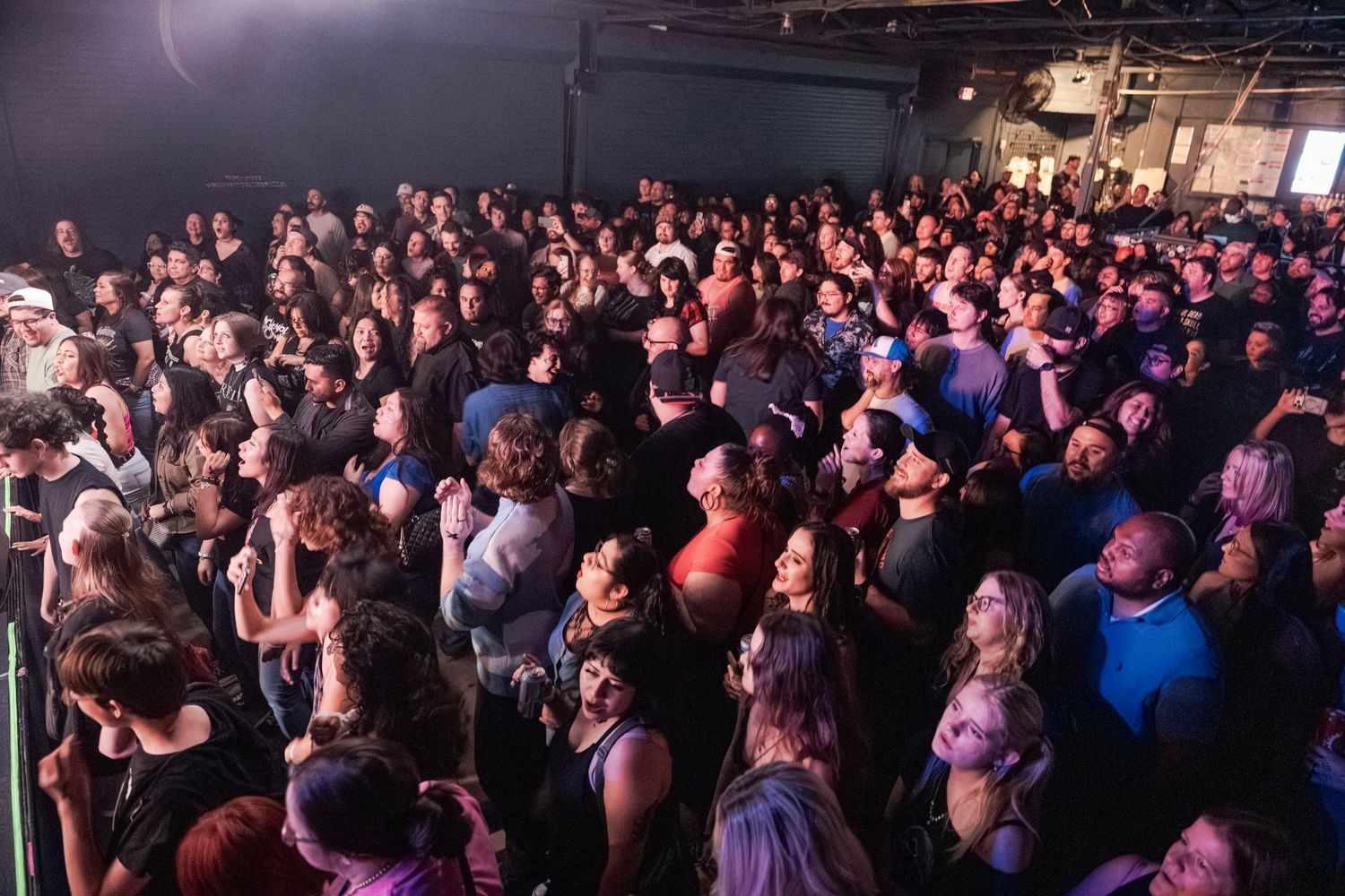 Large crowd of concert-goers packed together at an indoor music venue, enjoying a live performance.