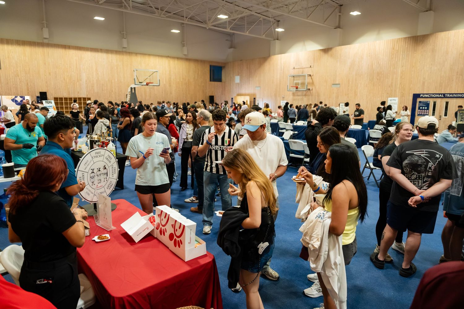 Crowded college fair event in a gymnasium with students browsing tables and meeting with representatives.