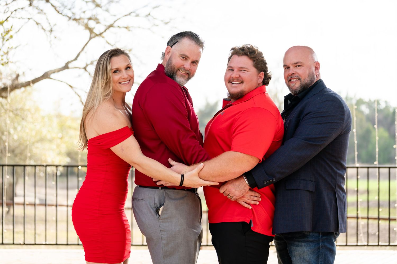 Four people in red and navy outfits posing together outdoors for a family portrait photo.