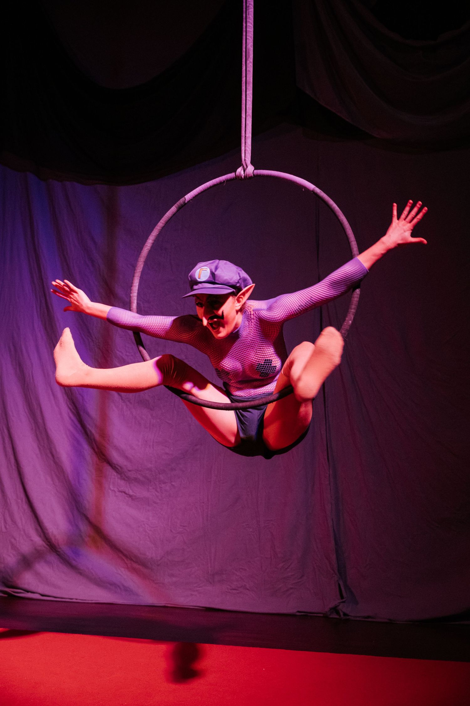 Aerial hoop performer balancing gracefully in a circular lyra ring under purple stage lighting.