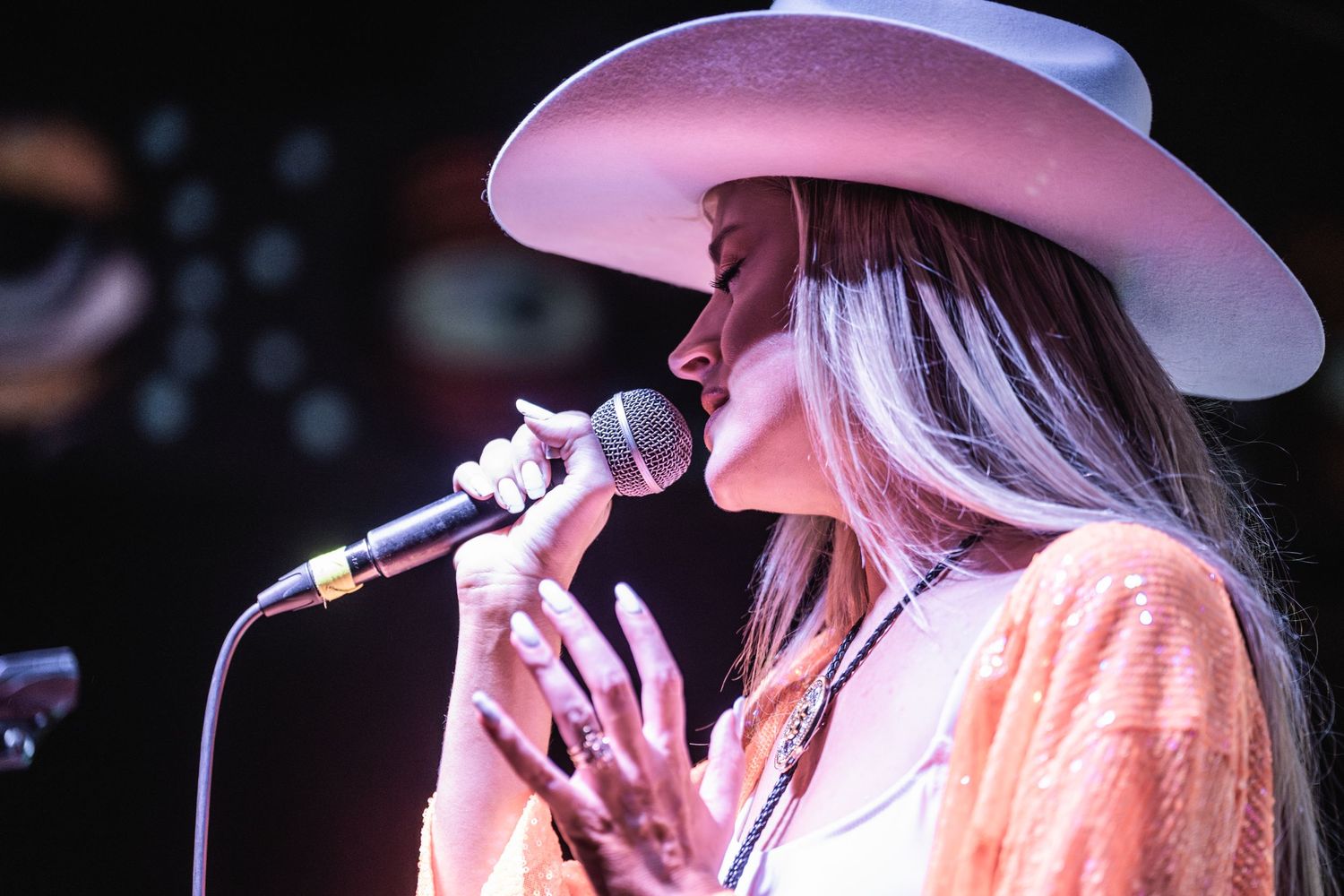 Country music performer in pink cowboy hat and white outfit singing on stage during live performance.
