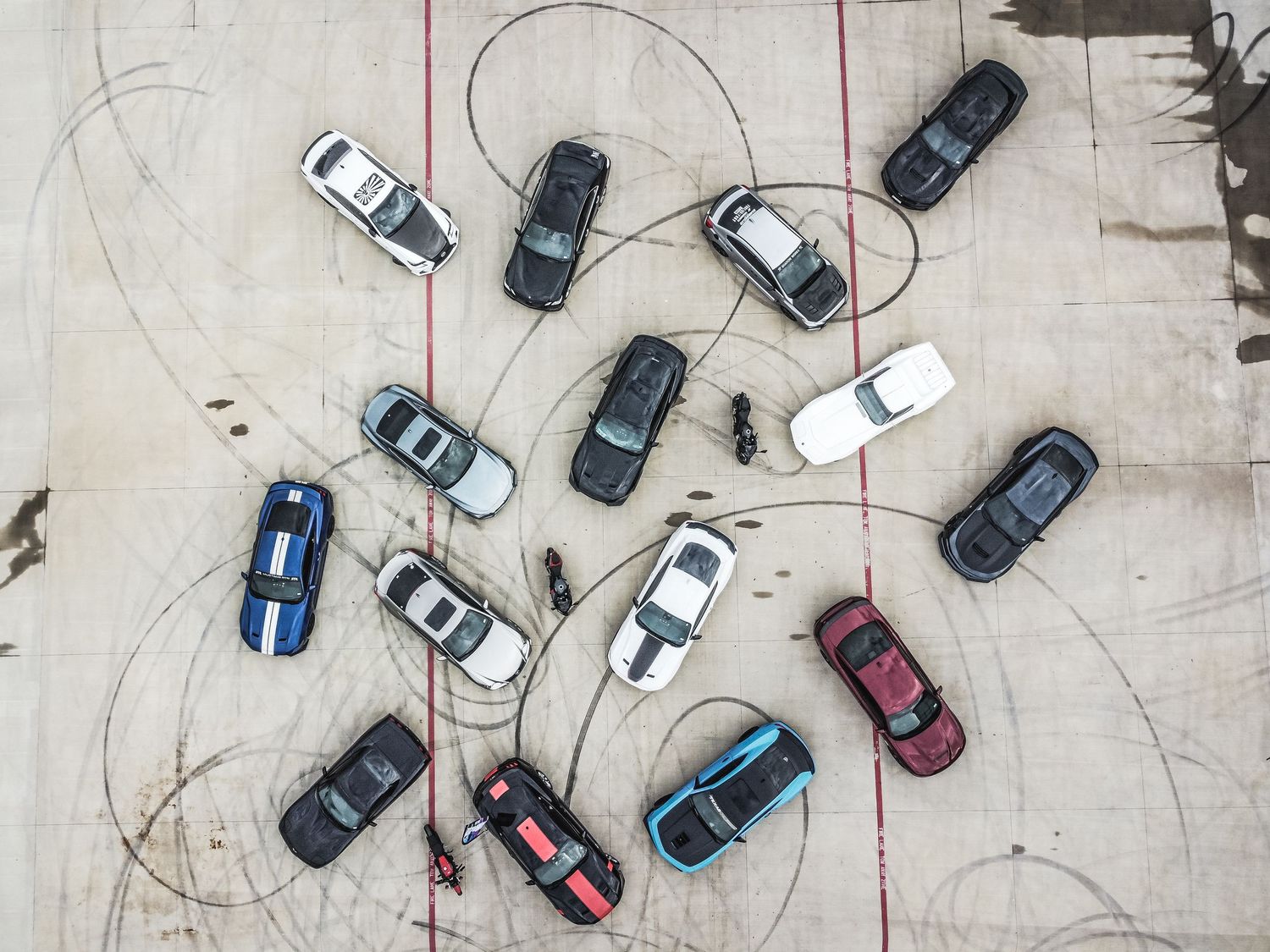 Birds-eye view of performance cars arranged in circular pattern with tire marks on concrete.