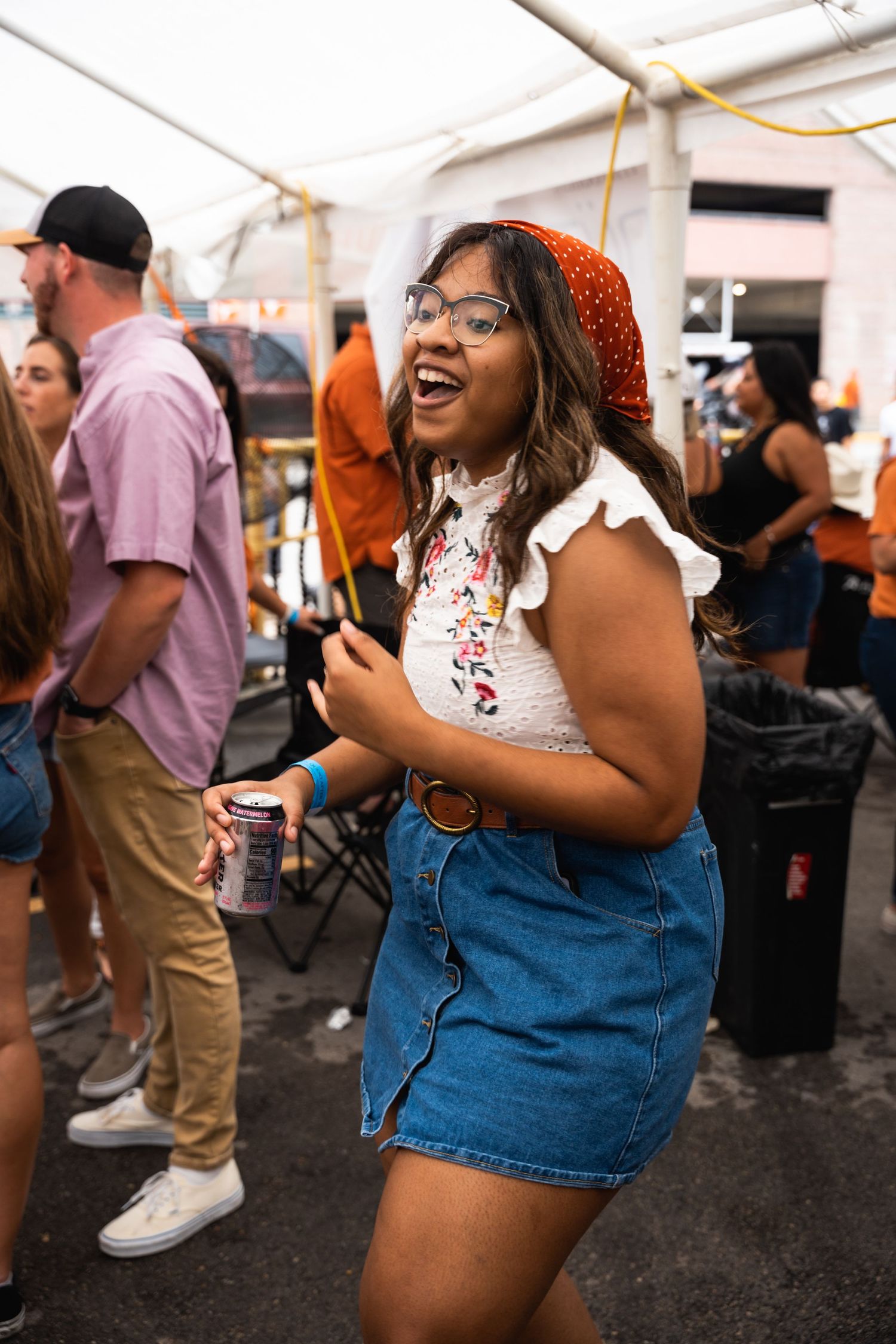 Person in orange headband and denim skirt dancing joyfully at an outdoor festival.