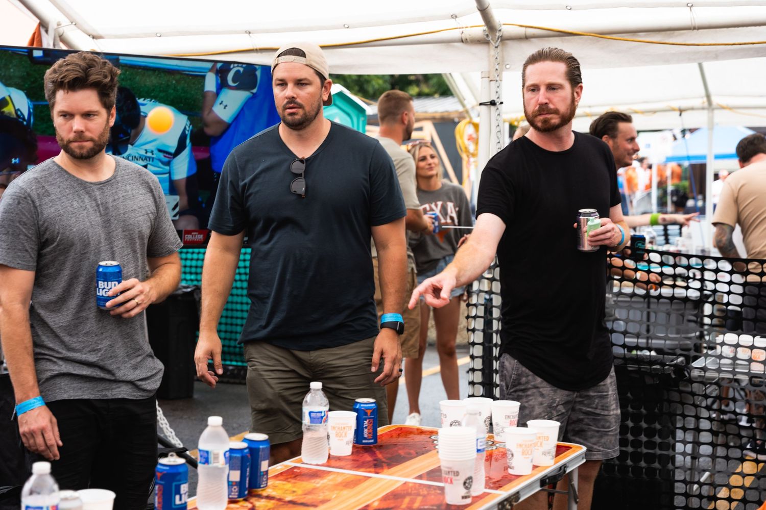 Three people in casual attire standing near a table at an outdoor event.