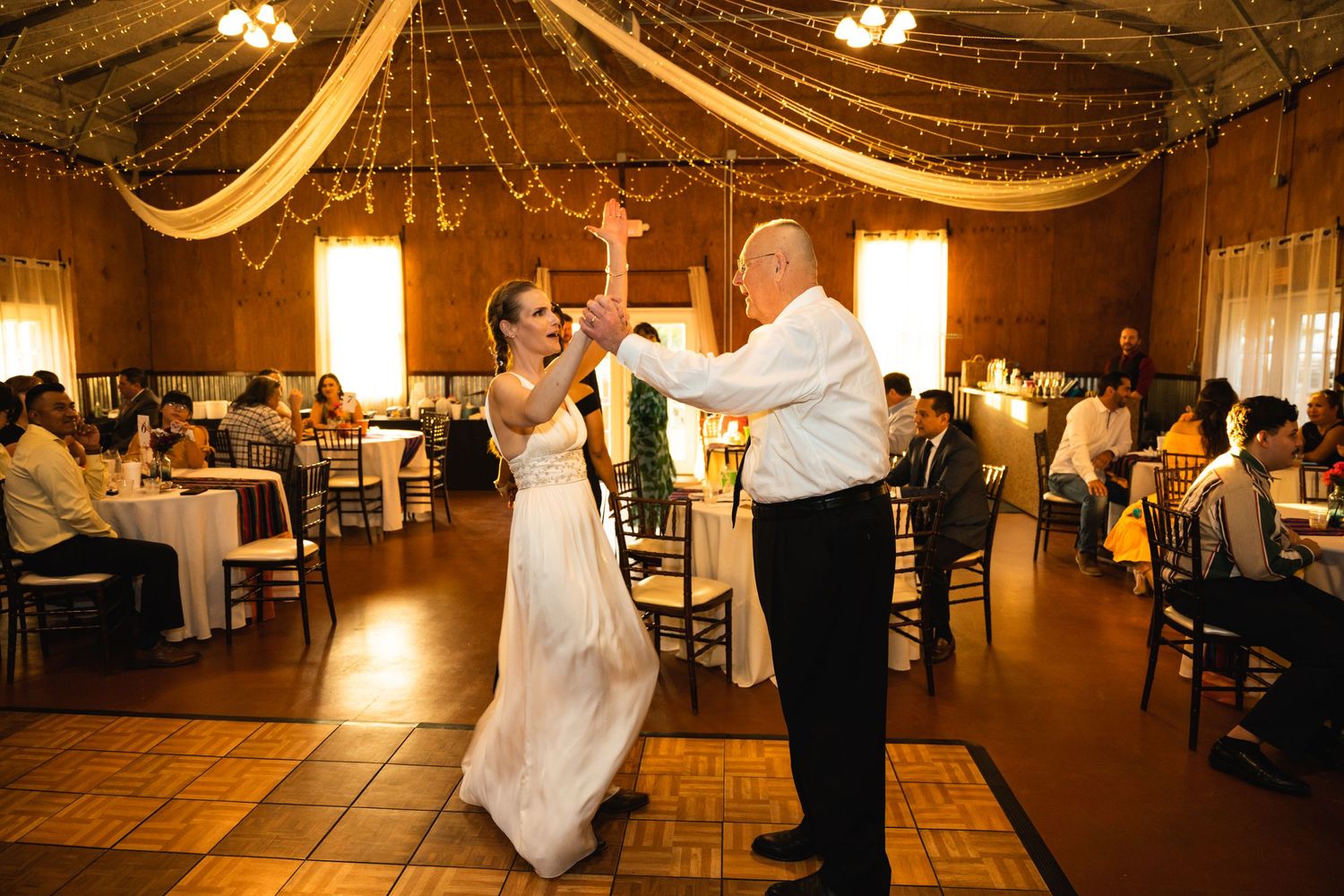 Dancing under string lights and draped fabric at elegant wedding reception venue.