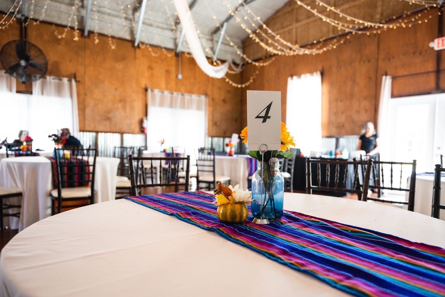 Wedding reception venue with colorful striped table runners and string lights decorating the rustic space.