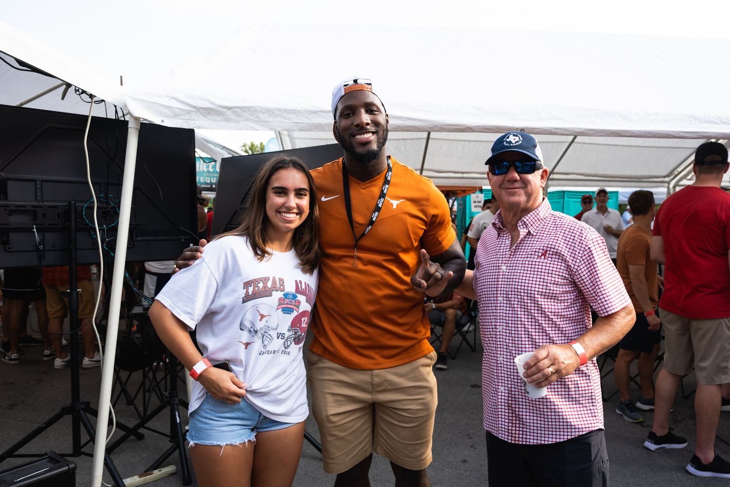 Three people pose together under a white tent at an outdoor event.