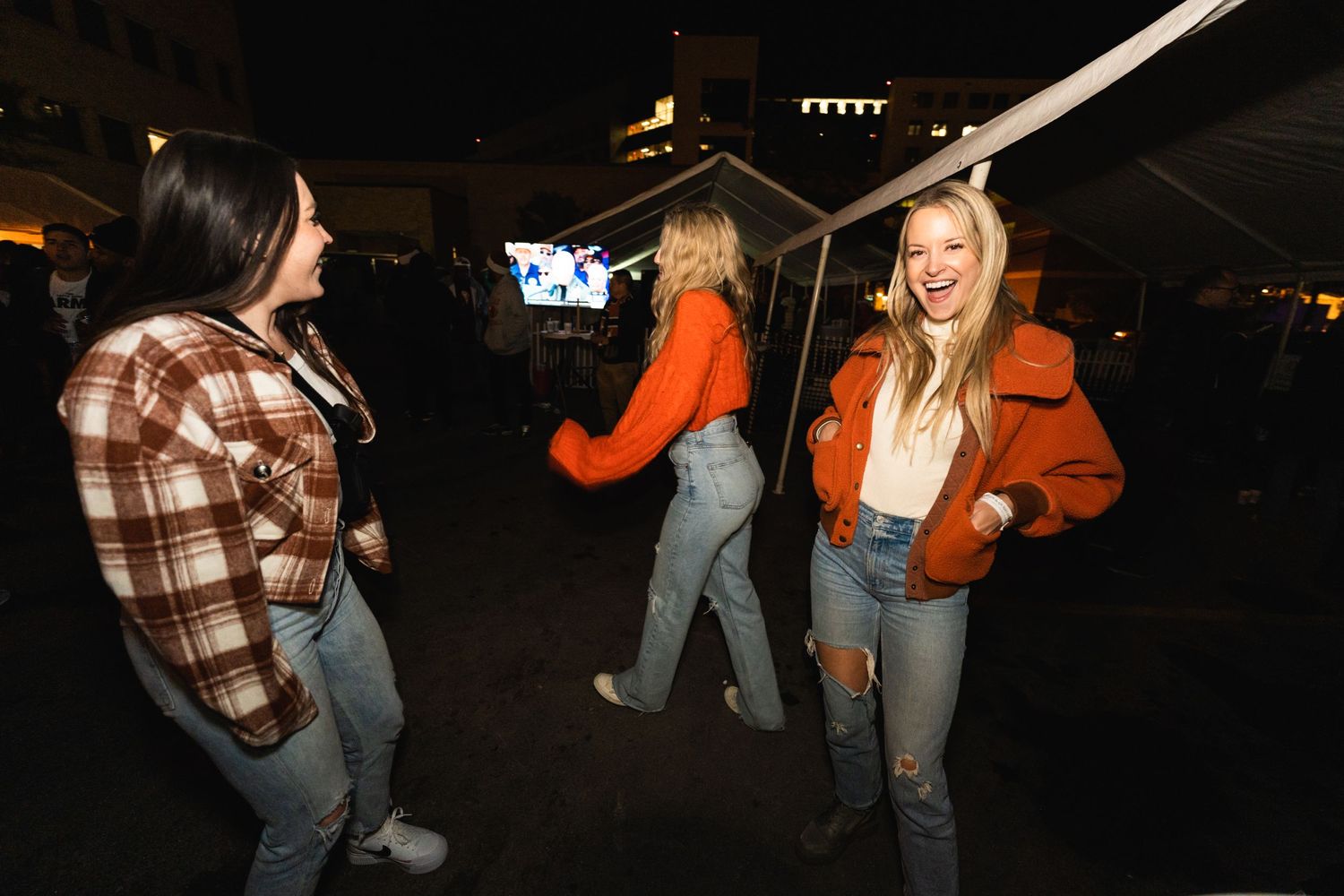 Friends in casual autumn attire dancing and socializing at outdoor nighttime gathering.