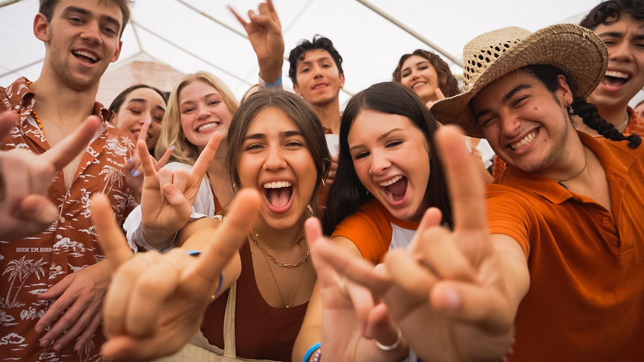 Enthusiastic group of friends showing hand gestures and smiling at outdoor celebration.