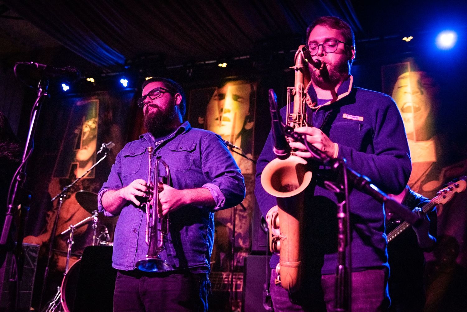 Two saxophone players perform on stage under blue lighting during a jazz performance.