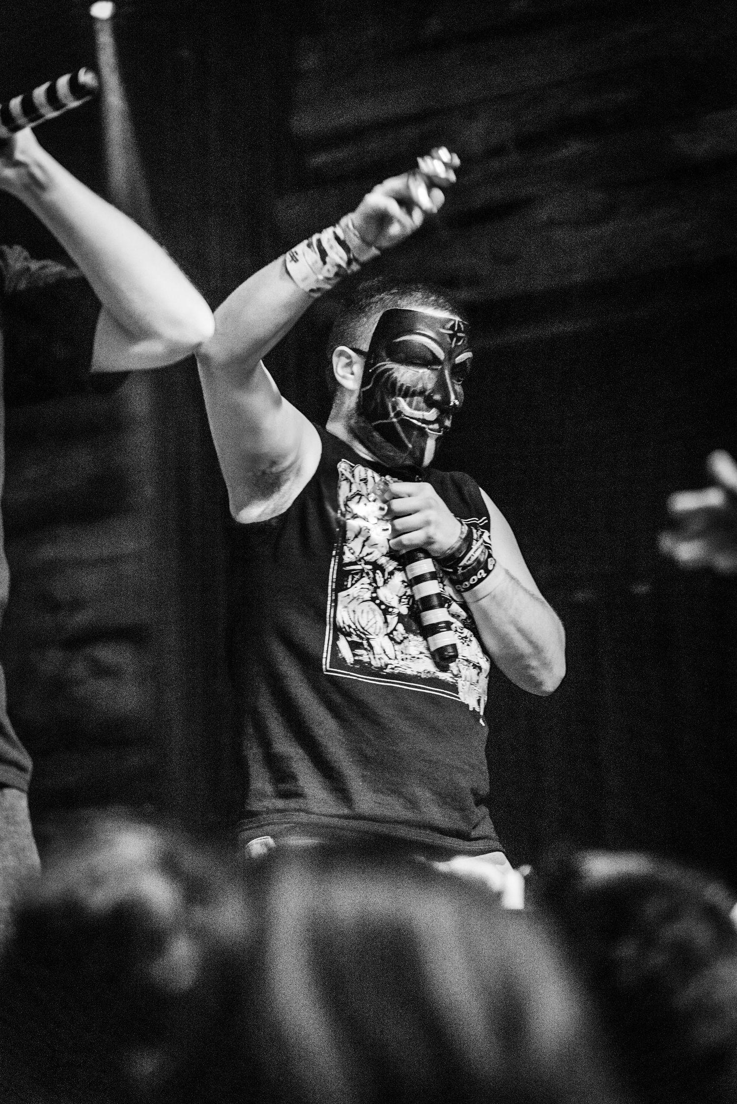 Performer in mask strikes dramatic pose during black and white concert photo.