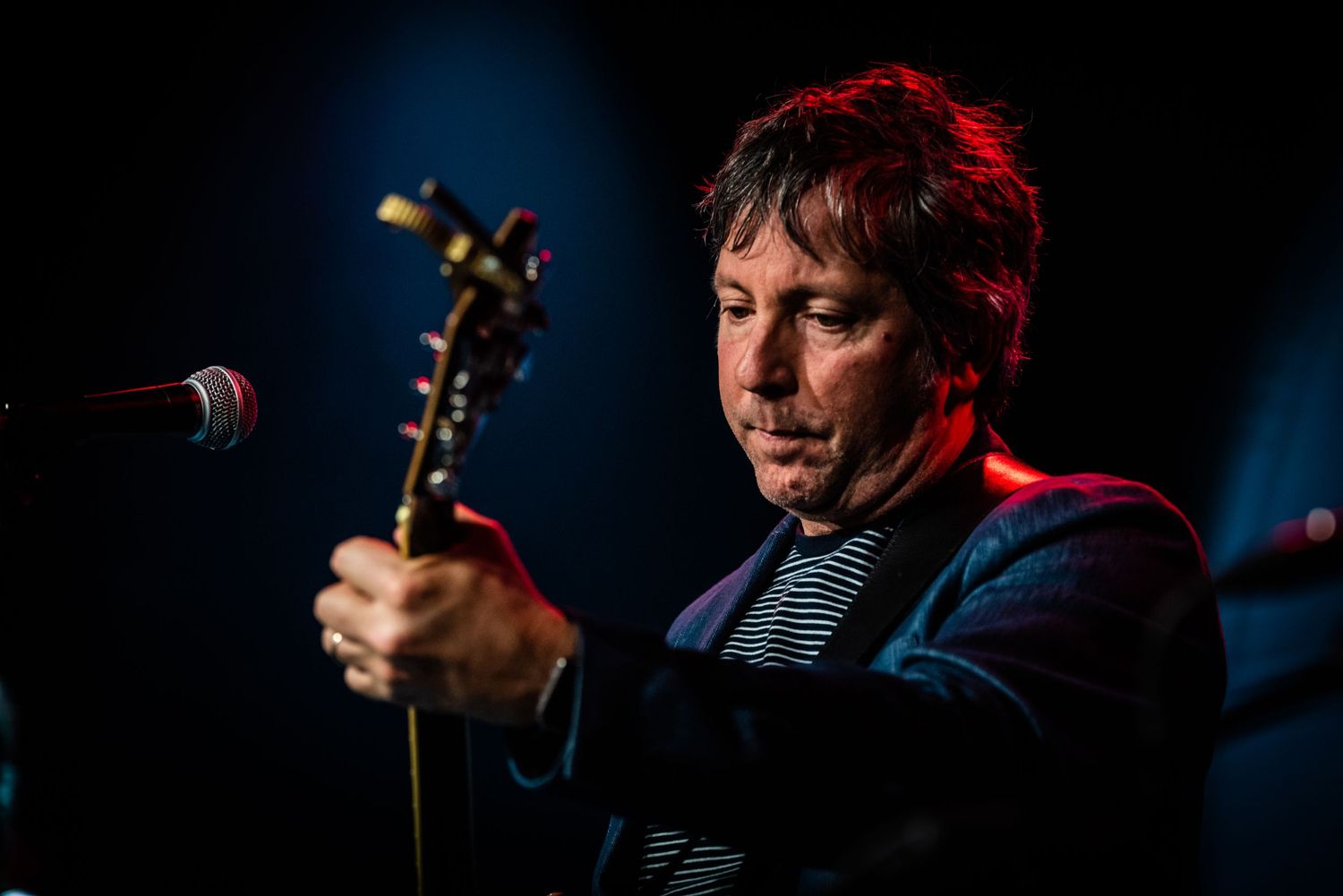 Side profile of guitarist performing under dramatic red and blue stage lighting.