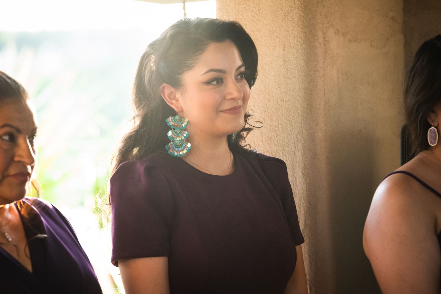 Wedding guest in formal attire with turquoise earrings watches ceremony indoors.