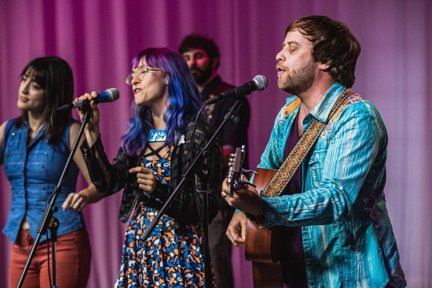 Folk band performs on stage with pink curtain backdrop.
