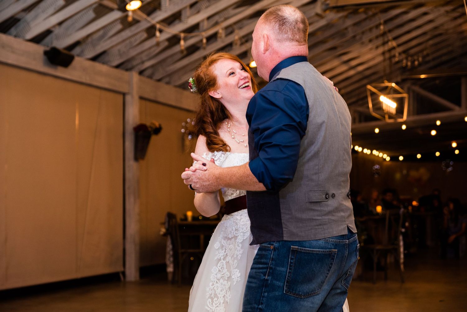 A couple shares their first dance in a rustic venue decorated with twinkling lights.