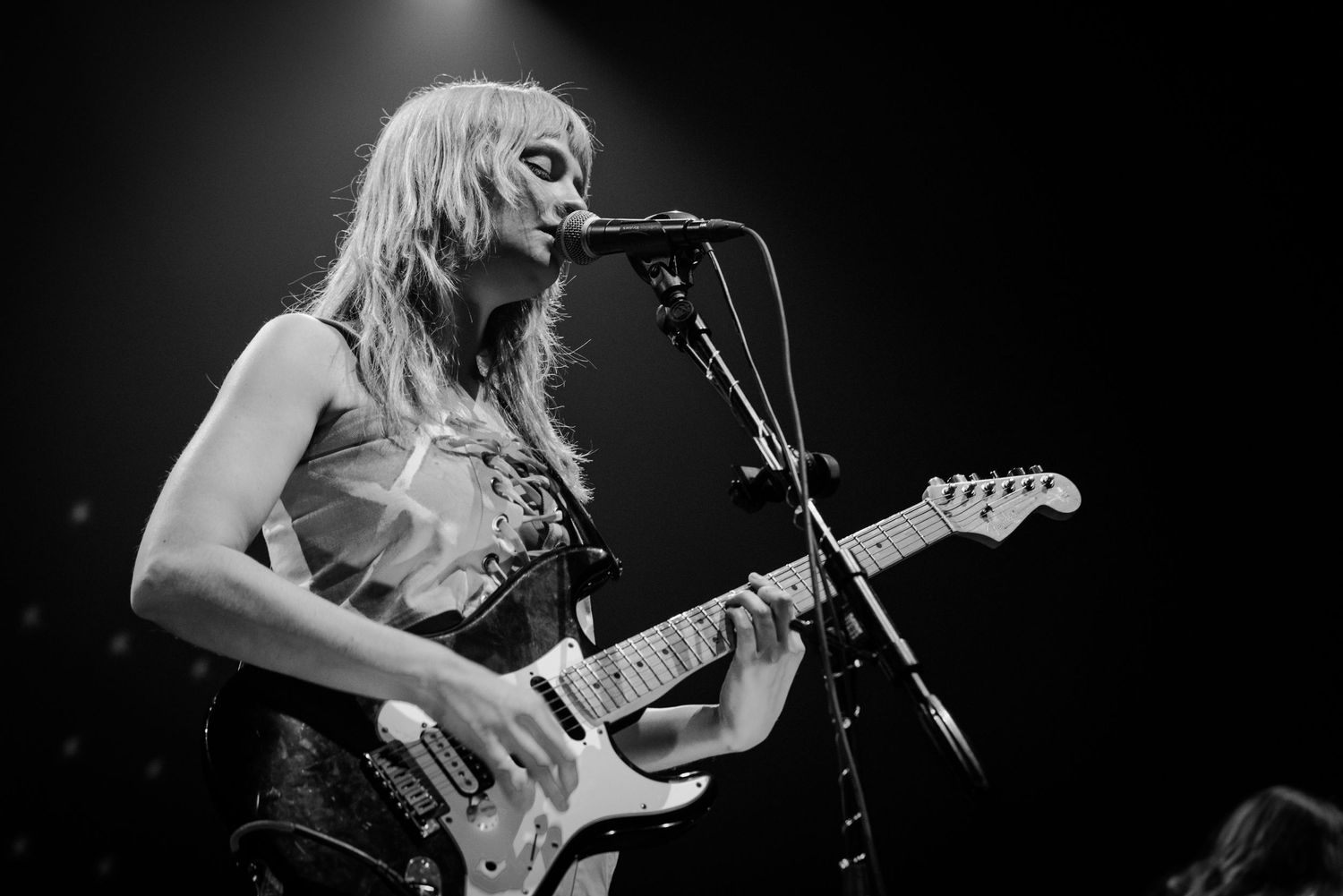 Black and white concert photo of guitarist performing with microphone on stage.