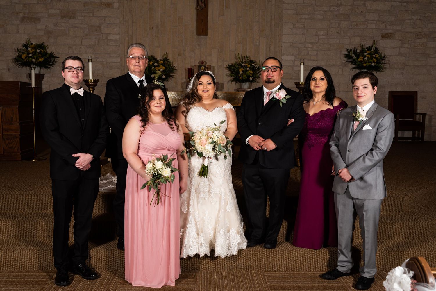 Formal wedding party group photo in church with mixed attire including pink and burgundy dresses.