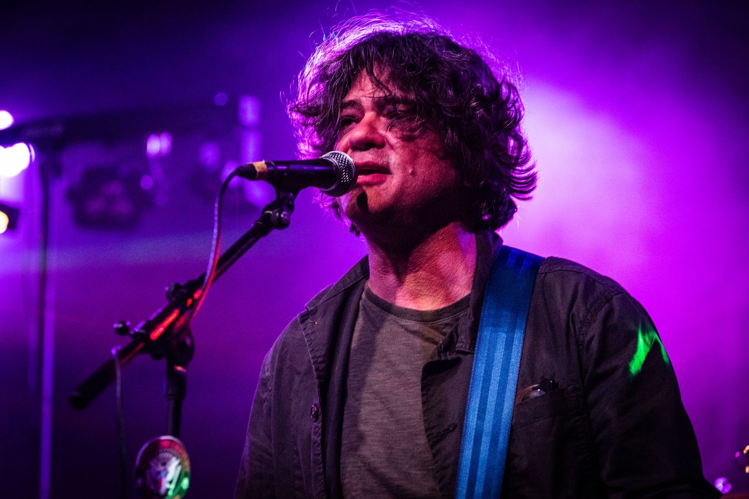 A rock musician sings and plays guitar under purple stage lighting.