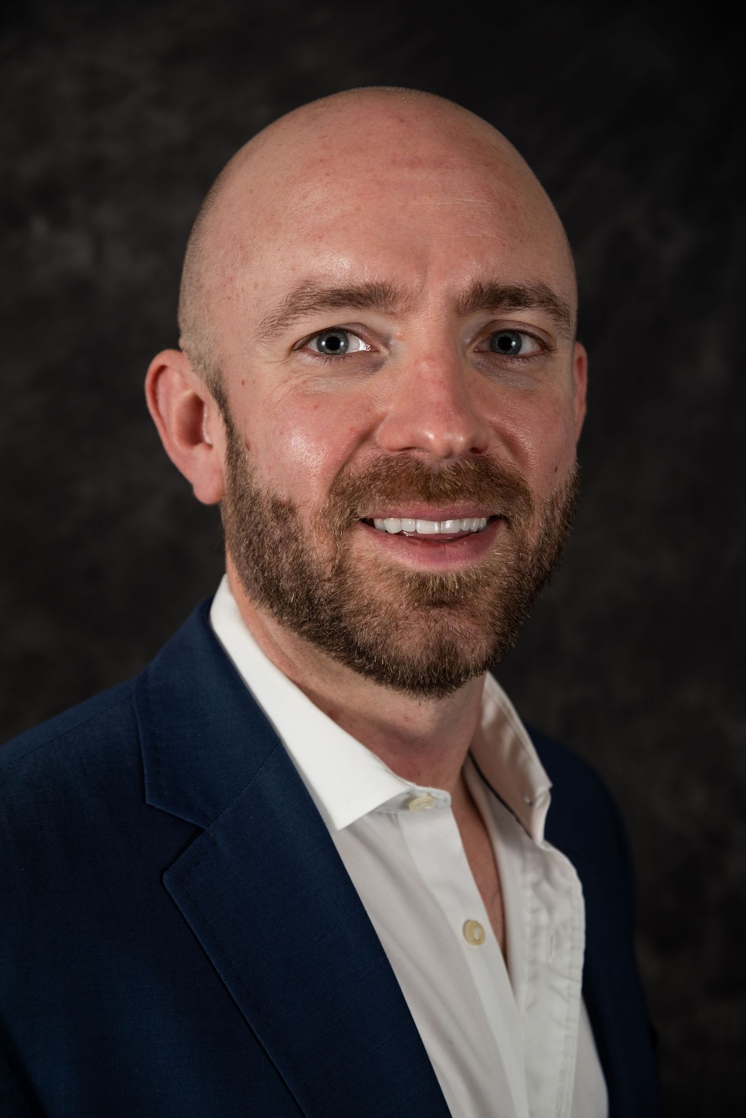 Professional studio portrait showing person in business casual attire with natural smile.