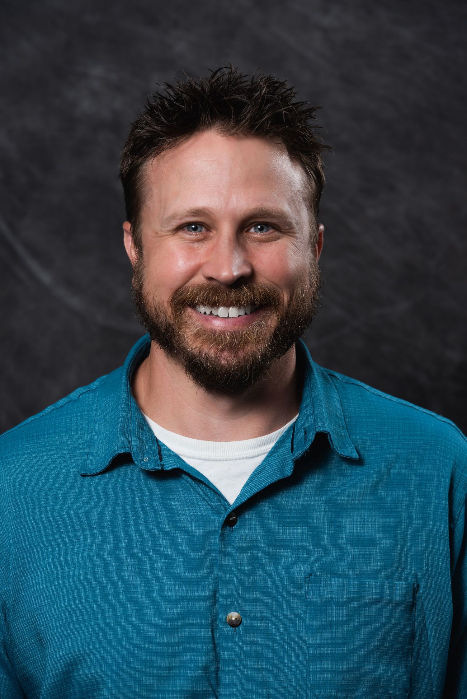 Professional headshot against dark background wearing blue collared shirt.