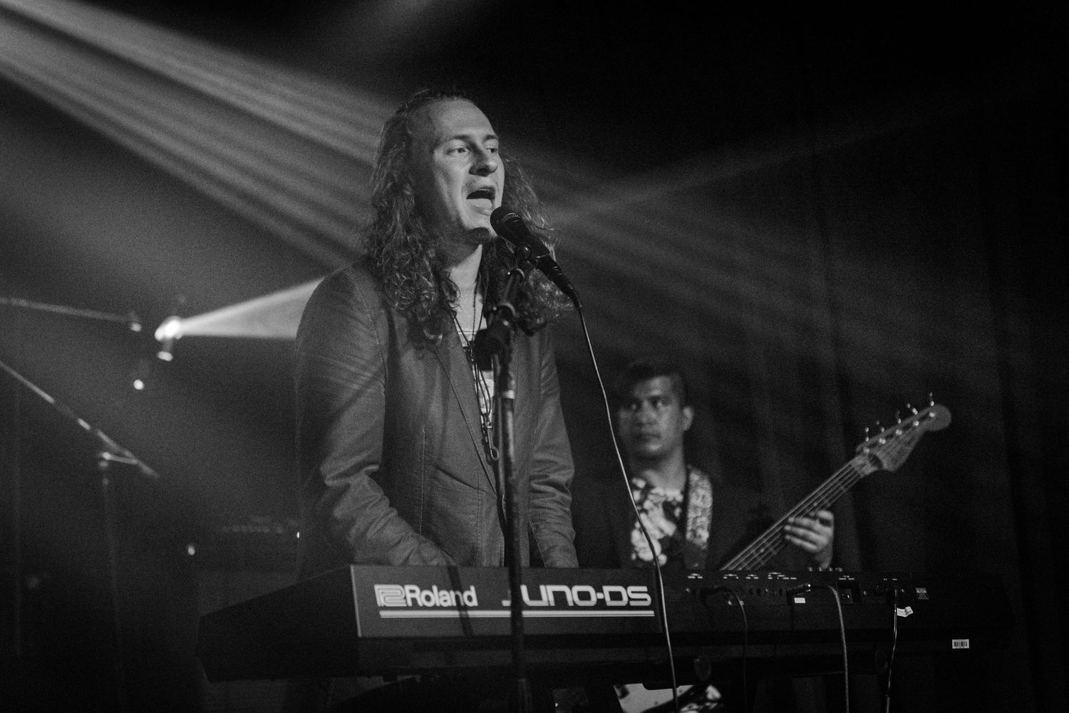 A performer sings while playing keyboard under stage lights.